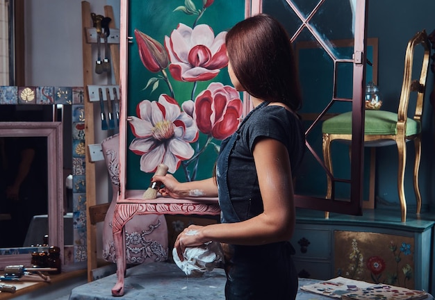 Une femme artiste peignant une étagère vintage rénovée dans l'atelier.