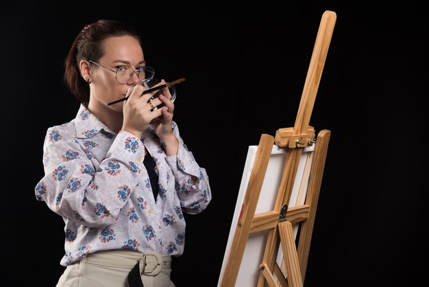 Femme artiste tenant le pinceau et boire du thé sur fond noir