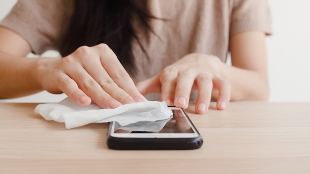 Femme asiatique à l'aide de vaporisateur d'alcool sur un téléphone portable propre avant de l'utiliser pour protéger le coronavirus Surface propre pour l'hygiène des femmes lorsque l'éloignement social reste à la maison et le temps d'auto-quarantaine.