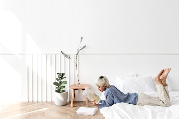 Femme asiatique aux cheveux blonds lisant un livre sur un matelas sur le sol