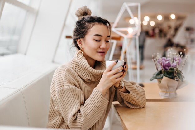 Femme asiatique blonde en pull surdimensionné tenant une tasse de thé blanc