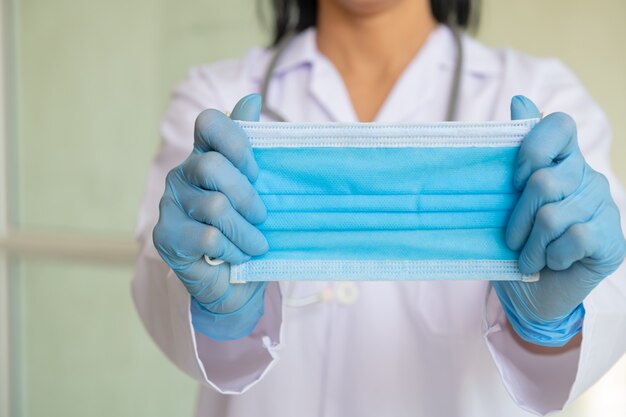 Femme asiatique en blouse de médecin ou blouse de laboratoire montrant comment porter correctement un masque chirurgical d'hygiène, démontrant la méthode pour sauver la santé de l'épidémie de virus et de l'air sale.