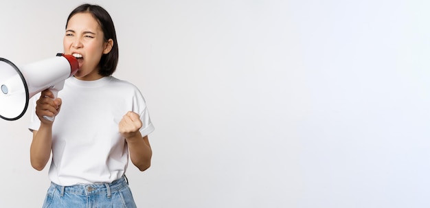 Femme asiatique confiante criant dans un mégaphone criant et protestant Girl activiste utilisant le haut-parleur pour parler plus fort debout sur fond blanc