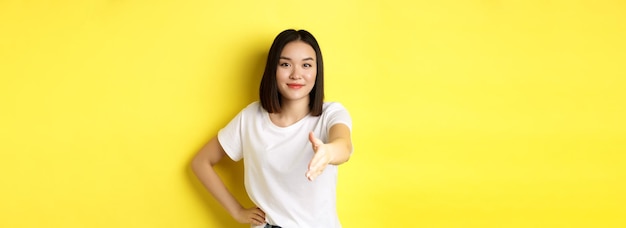 Photo gratuite une femme asiatique confiante en t-shirt blanc tend la main pour une poignée de main et un geste de salutation disant hel