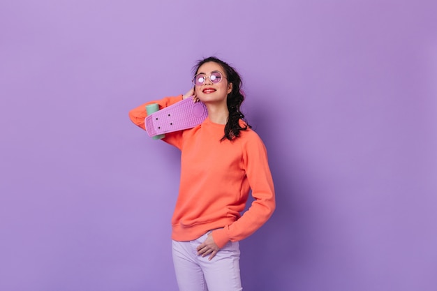 Femme asiatique dans des verres tenant le longboard. Photo de Studio de femme japonaise avec skateboard isolé sur fond violet.