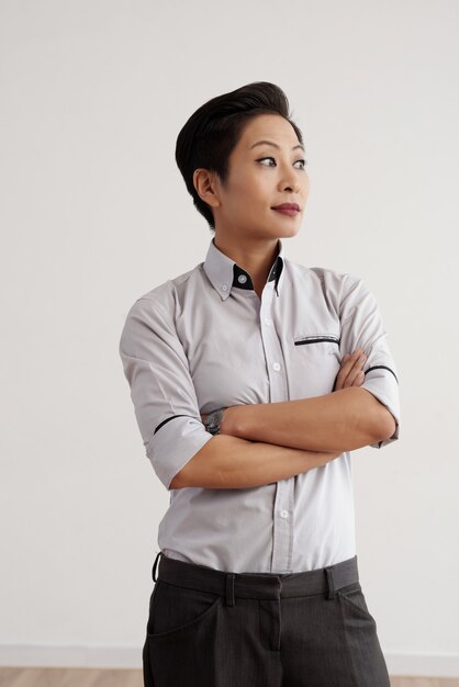 Femme asiatique élégante en pantalon et chemise posant en studio avec bras croisés