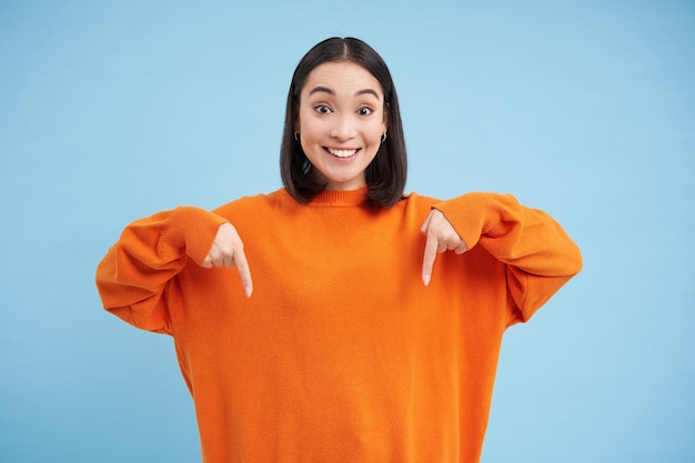 Photo gratuite une femme asiatique excitée pointant vers le bas montre une publicité ci-dessous avec un sourire heureux regarde là le geste stan