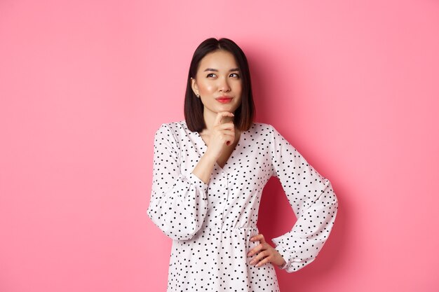 Femme asiatique heureuse réfléchie prenant une décision souriante satisfaite et regardant le logo en haut à gauche pensant...