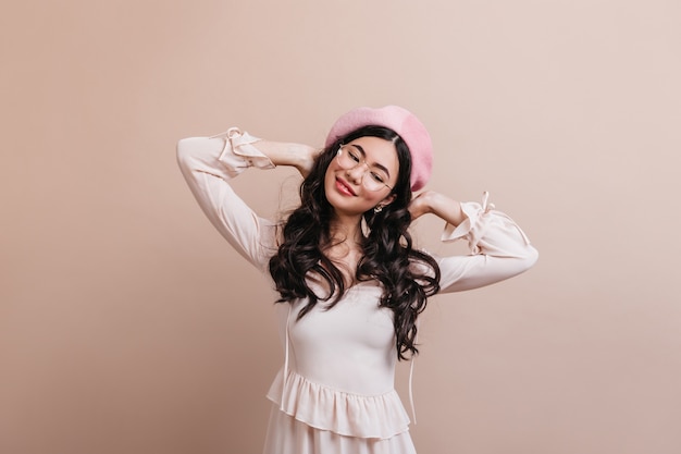 Femme asiatique insouciante portant béret français. Femme chinoise aux cheveux longs positive debout sur fond beige.