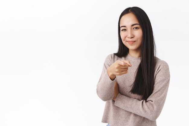 Femme asiatique joyeuse et confiante faisant le choix, vous choisissant, pointant la caméra et souriant heureusement, invitez à un entretien pour travailler dans son entreprise