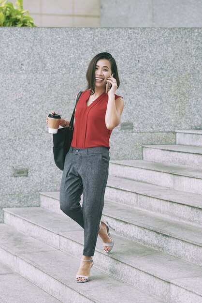 Femme asiatique joyeuse qui marche dans les escaliers en plein air et parler au téléphone mobile