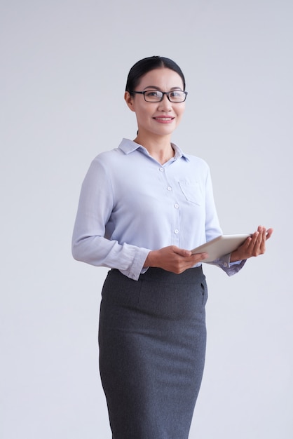 Femme asiatique à lunettes, chemisier élégant et jupe qui pose en studio avec tablette