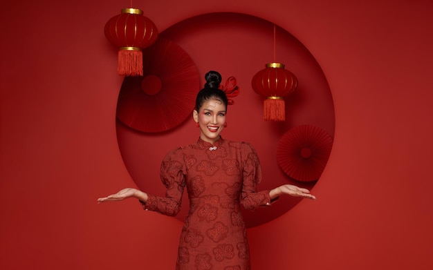 Une femme asiatique portant une robe traditionnelle cheongsam qipao avec un geste de bienvenue au Nouvel An chinois 2024