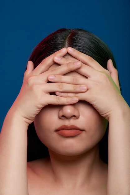 Femme asiatique qui pose en studio et qui couvre les yeux avec des doigts imbriqués