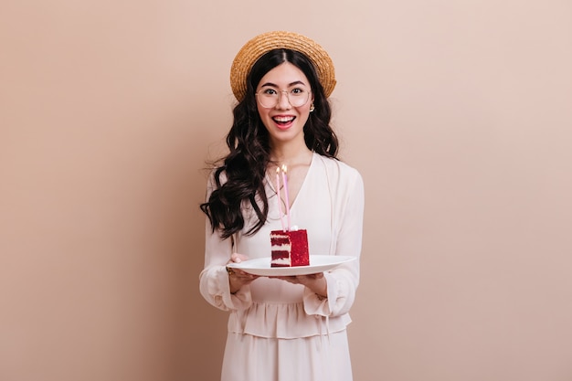 Femme asiatique regardant la caméra avec le sourire. Heureuse femme japonaise au chapeau de paille tenant le gâteau.