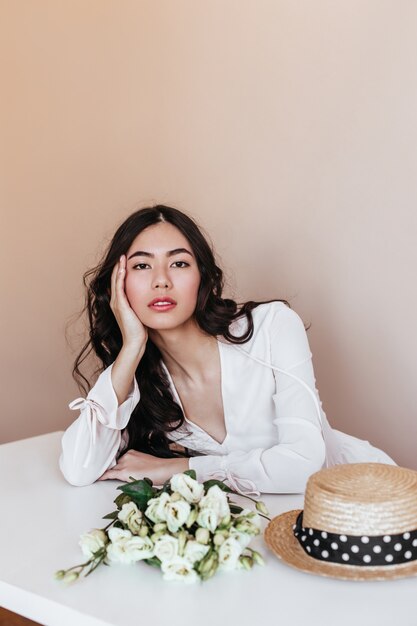 Femme asiatique en robe blanche avec des fleurs en regardant la caméra. Vue de face du charmant modèle féminin chinois posant avec bouquet d'eustoma.