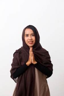 Une femme asiatique en robe musulmane se lève dans une pose de salutation aux mains de namaste pour saluer l'aïd fitr