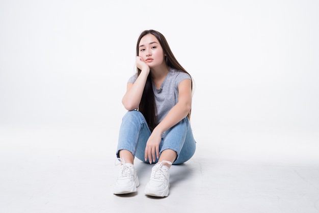 Femme asiatique s'ennuie assis sur le sol isolé sur un mur blanc.