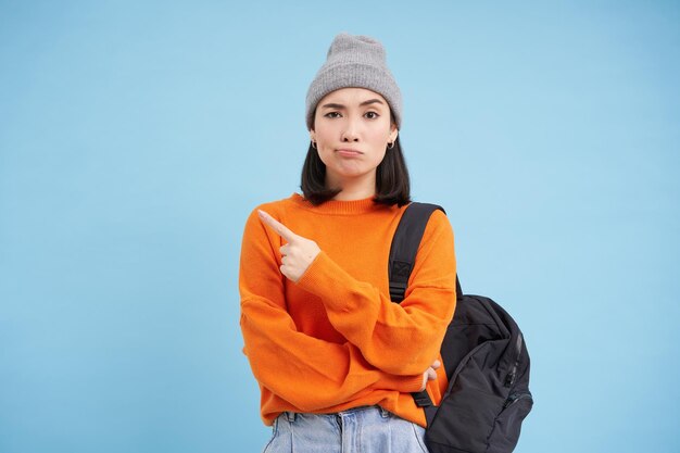 Une femme asiatique sceptique pointant vers la gauche sur une bannière étrange semble douteuse se dresse sur fond de studio