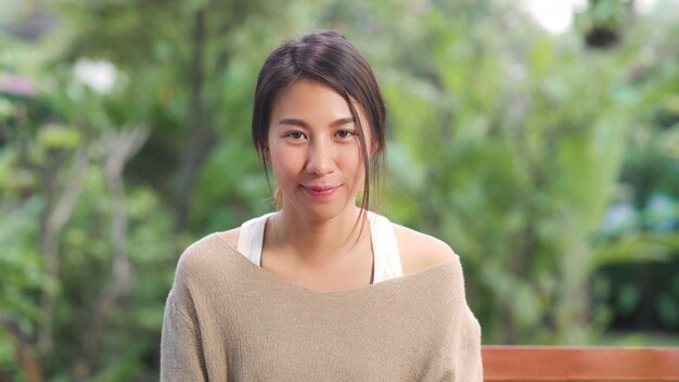 Femme asiatique se sentant heureuse en souriant et en regardant pendant que vous vous détendez sur la table dans le jardin à la maison le matin. Femmes de mode de vie se détendre à la maison concept.