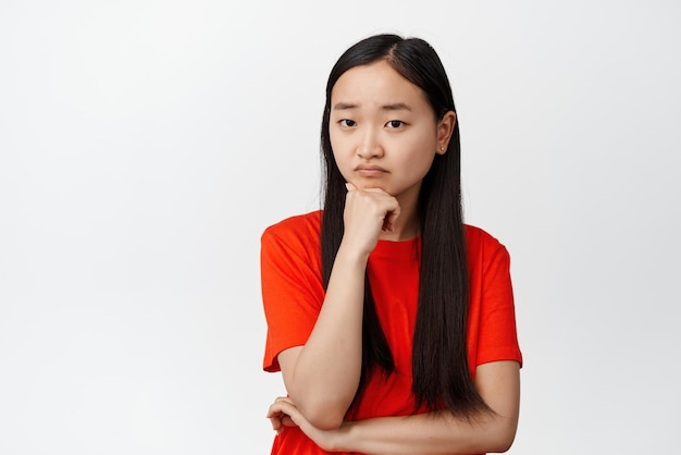 Femme asiatique sombre regardant la caméra troublée en écoutant quelque chose de bouleversant en détresse debout sur fond blanc