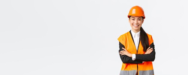 Femme asiatique souriante et confiante, chef de la direction d'un ouvrier du bâtiment en casque de sécurité croisé