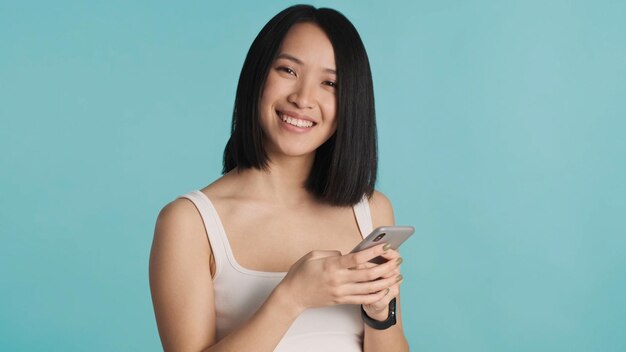 Femme asiatique tapant un message texte sur un smartphone profitant d'une communication en ligne sur fond coloré Femme positive regardant la caméra