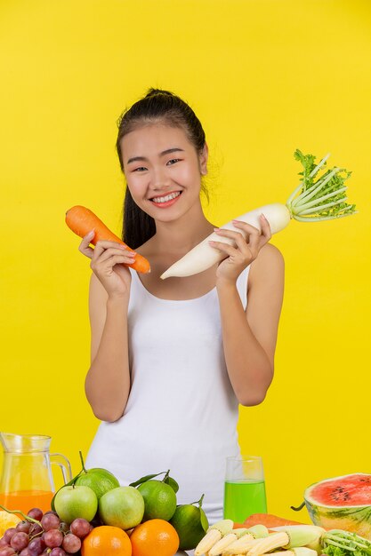 Femme asiatique tenant une carotte de la main droite Tenez le radis de la main gauche et sur la table de nombreux fruits.