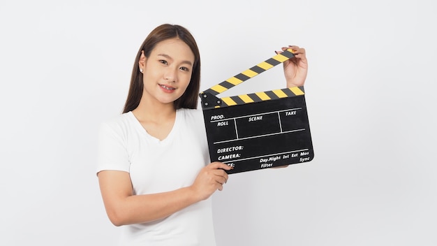 Une femme asiatique tient un clap noir ou une ardoise de film ou un clap et porte des bretelles sur fond blanc.