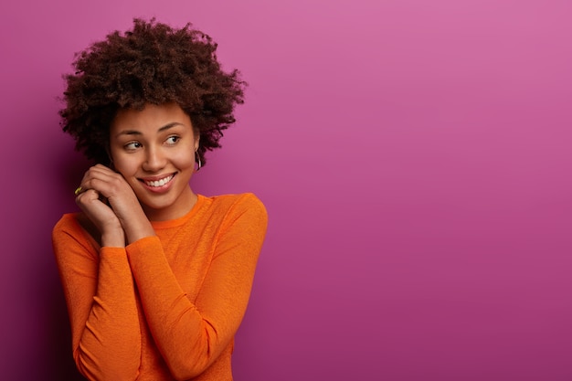 Photo gratuite femme assez calme avec une coiffure afro, regarde doucement de côté, garde les mains près du visage