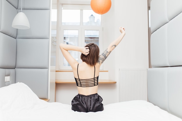 femme assise au bord du lit et étirant ses bras pour se détendre le matin après se réveiller le matin