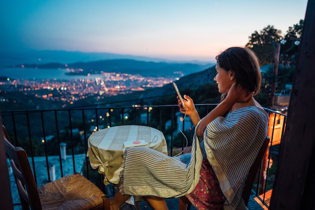 Femme assise sur le balcon, en arrière-plan la ville de nuit