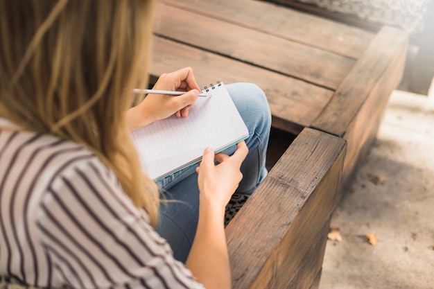 Femme assise sur un banc, écrivant sur un cahier avec un crayon