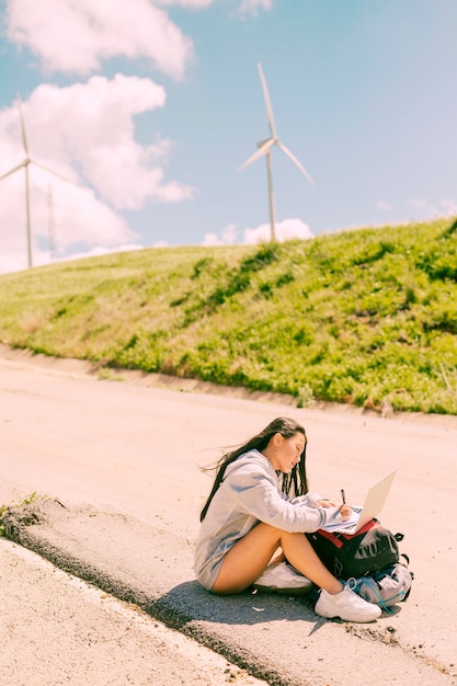 Femme assise sur le bord de la route et travaillant sur un ordinateur portable placé sur des sacs à dos