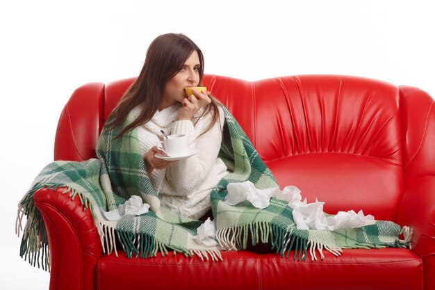 Femme assise sur le canapé avec un citron dans la bouche