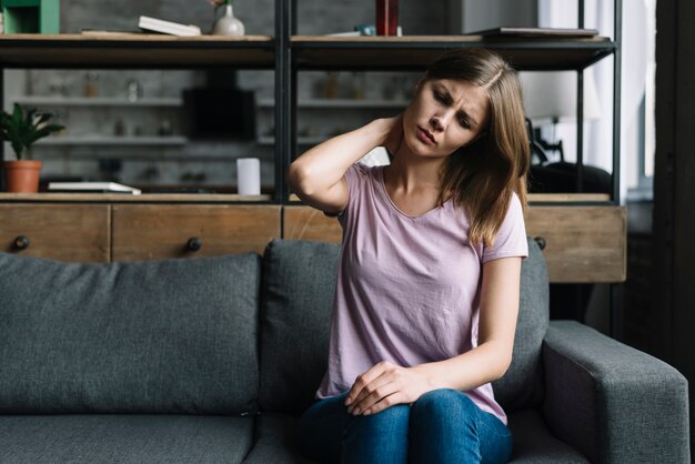 Femme assise sur un canapé souffrant de douleurs au cou