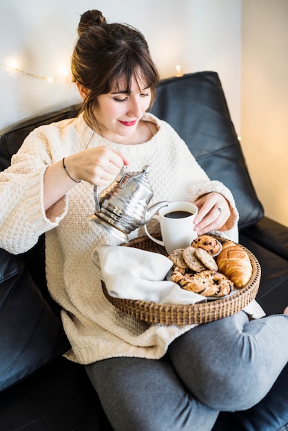 Femme assise sur un canapé, verser le thé dans une tasse