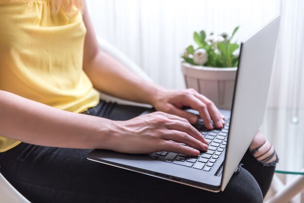 Femme assise sur une chaise à l'aide d'un ordinateur portable sur ses genoux