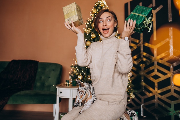 Femme assise sur une chaise de poney en bois près du sapin de Noël