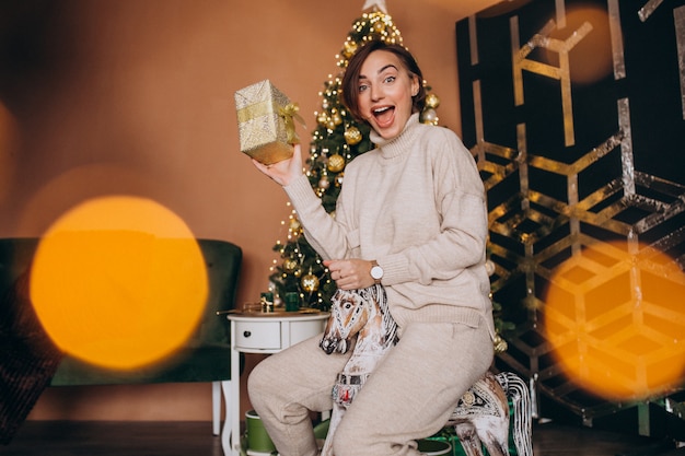 Femme assise sur une chaise de poney en bois près du sapin de Noël