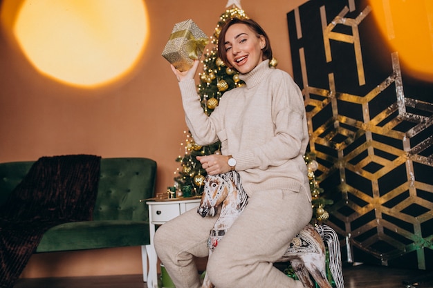 Femme assise sur une chaise de poney en bois près du sapin de Noël