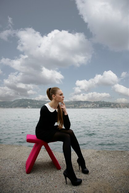 Femme assise sur une chaise rose à la plage