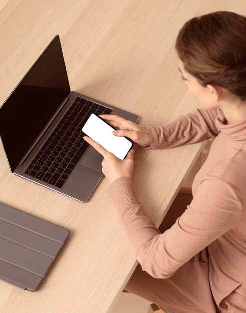 Femme assise à côté de son ordinateur portable et à l'aide de smartphone