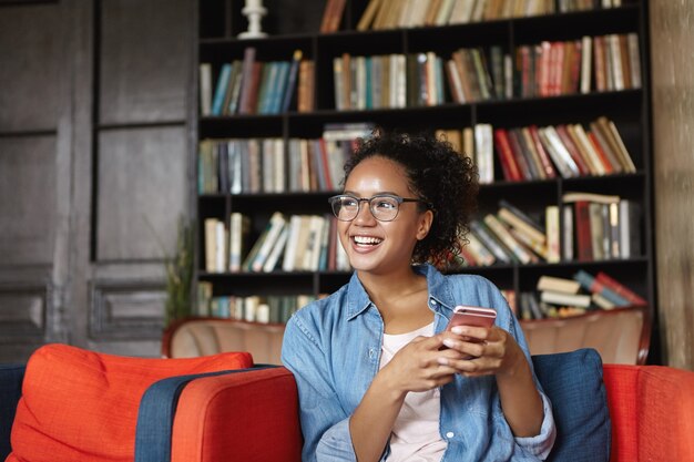 Femme assise dans une bibliothèque avec son téléphone