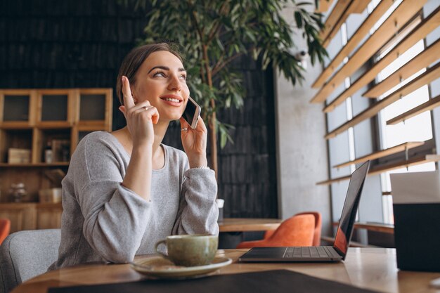 Femme assise dans un café, buvant du café et travaillant sur un ordinateur