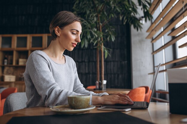 Femme assise dans un café, buvant du café et travaillant sur un ordinateur