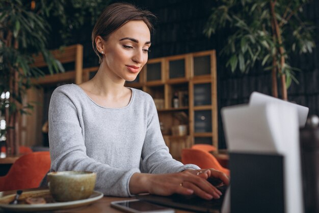 Femme assise dans un café, buvant du café et travaillant sur un ordinateur
