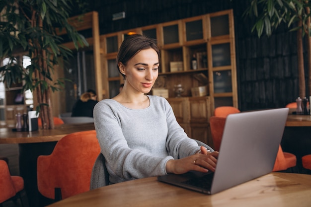 Femme assise dans un café, buvant du café et travaillant sur un ordinateur