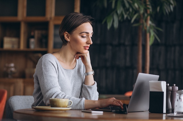 Femme assise dans un café, buvant du café et travaillant sur un ordinateur