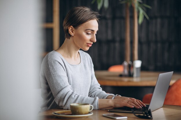 Femme assise dans un café, buvant du café et travaillant sur un ordinateur